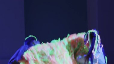 İki küçük gülümseyen kız arkadaş neon ışıkta renkli kurdeleler kusuyor.