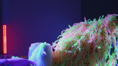 Küçük çocuklar ve animasyoncular neon odaya renkli kurdeleler fırlatıyorlar.