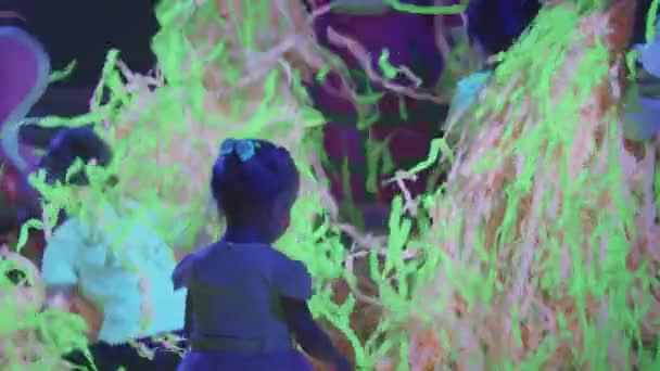 Små barn och animatörer som kastar upp färgglada band i neonrummet medan showen — Stockvideo