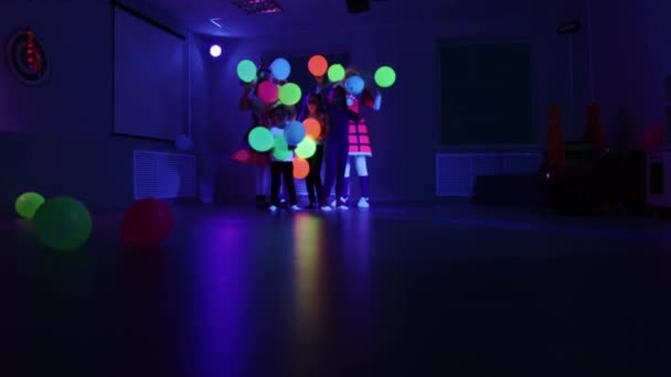 Födelsedag firande - små barn och animatörer som håller och kräks upp ballonger i neon belysning — Stockvideo