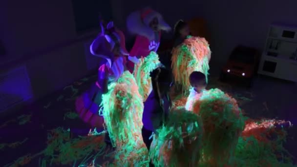Doğum günü kutlaması - küçük çocuklar ve animasyoncular yeşil ve turuncu kurdeleleri neon ışıkla fırlatıyorlar — Stok video