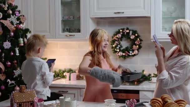 Щасливе сімейне Різдво - дівчина виймає лист для випічки і її мама фотографує її — стокове відео