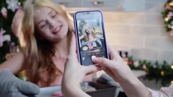 Joyeux Noël de famille une fille debout avec plaque à pâtisserie et sa mère prenant des photos d'elle au téléphone — Video