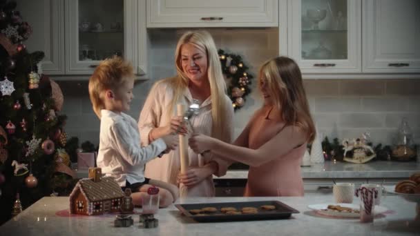 Rodzinne święta - mama i jej dzieci pieką ciasteczka w kuchni - dzieci bawiące się chochlikami — Wideo stockowe
