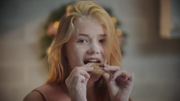 Rodzinne święta - uśmiechnięta dziewczyna pokryta mąką jedząca ciasteczka — Wideo stockowe