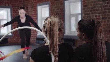 Jimnastik - genç kadın stüdyoda diğer kadınlara kurdeleyle jimnastik egzersizleri gösteriyor.