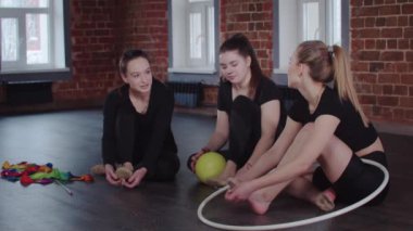 Jimnastik - üç akrobatik kadın yerde bir top ve bir potayla jimnastik gösterisi ve konuşma için oturuyorlar - hazırlanıyorlar.