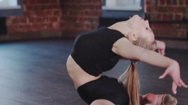 Jimnastik - kurbağa pozisyonunda oturan ve sırtını arkaya doğru eğen sarışın genç kadın - kameraya bakıyor