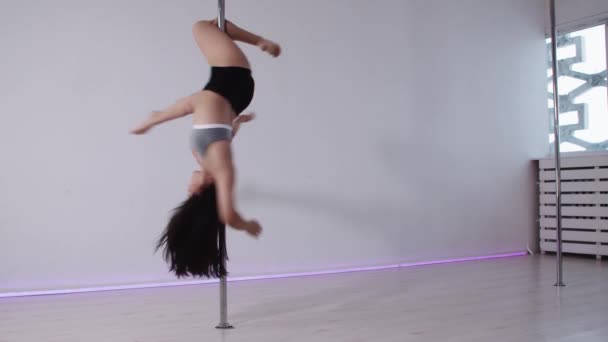 Pole dance ve studiu - brunetka žena rotující na tyči vzhůru nohama — Stock video