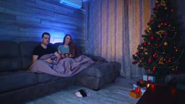 Pasangan muda duduk di sofa di bawah selimut dan bermain game di TV — Stok Video