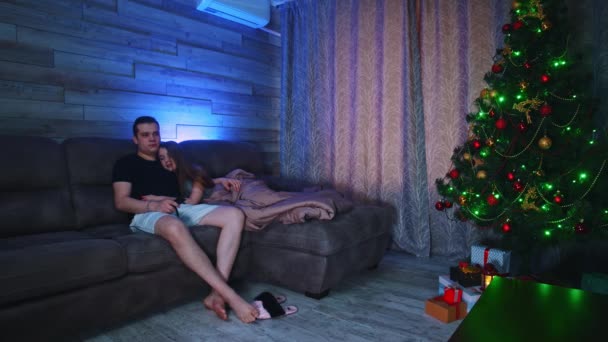 Junges Paar sitzt auf einer Couch - Frau schläft auf der Schulter ihrer Freunde ein und umarmt sie beim Fernsehen — Stockvideo