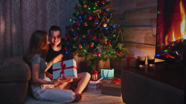 Pasangan muda duduk di lantai dekat pohon dan bertukar hadiah pada hari Natal — Stok Video