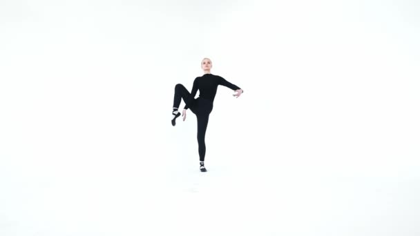 Jeune femme blonde ballerine levant sa jambe contre son corps et le tenant sur fond blanc — Video