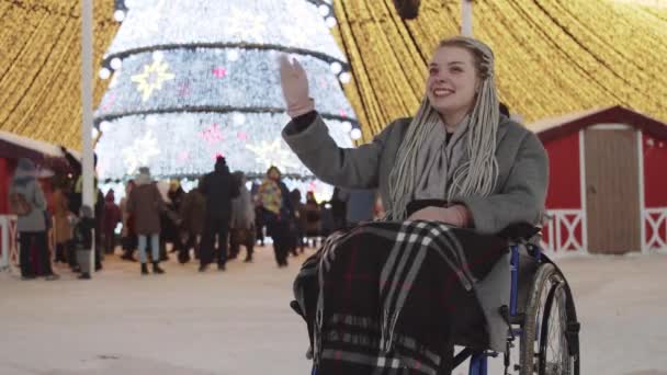 Giovane donna su una sedia a rotelle alla festa di Natale per le strade - agitando mano al suo ragazzo e lui viene da lei — Video Stock