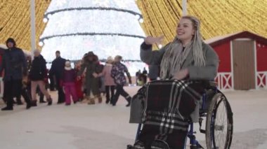 Noel partisinde tekerlekli sandalyedeki genç bir kadın sokakta erkek arkadaşına el sallıyor ve erkek arkadaşı ona gelip yanağından öpüyor.