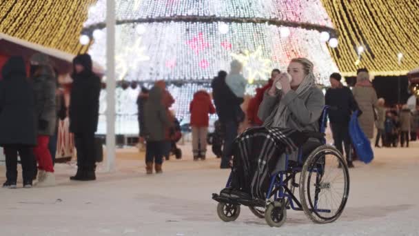 Een jonge vrouw met grijze dreadlocks in een rolstoel op een helder kerstfeest buiten - koffie drinken uit de beker — Stockvideo