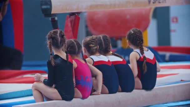 Dziewczynki siedzą na poprzeczce i czekają na swoją kolej na turnieju gimnastycznym. — Wideo stockowe