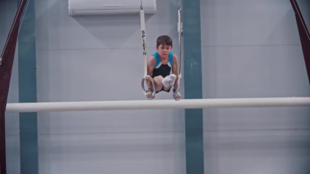 РОССИЯ, КАЗАН 27-12-20: Маленький гимнастический мальчик, тренирующийся на спортивных кольцах со своим тренером - сильно опирается на кольца и удерживает позицию — стоковое видео