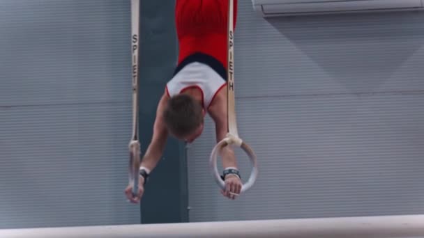 RUSSIA, KAZAN 27-12-20: kleine gymnastiekjongen die binnen op de sportringen traint - leunt zwaar op de ringen en houdt de positie — Stockvideo