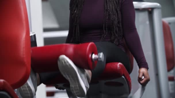 Une femme afro-américaine travaillant dans un gymnase sur un équipement d'exercice de jambe — Video