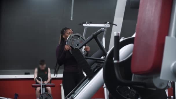 Una mujer negra montando un peso en un equipo de ejercicio — Vídeo de stock