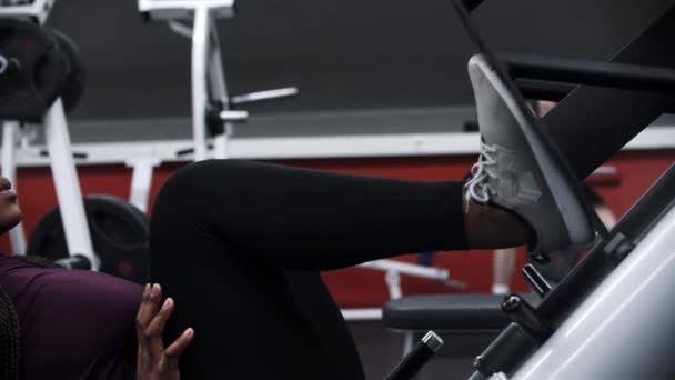 Una donna nera che allena le gambe su un attrezzo da ginnastica in palestra — Video Stock