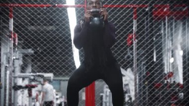 Spor salonunda ağırlığı ile çömelmiş Afro-Amerikalı bir kadın.
