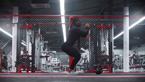 An african-american with pumped butt sportive woman squatting in a modern gym — Vídeos de Stock