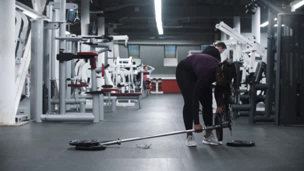 Seorang wanita Afrika-Amerika membongkar dumbel pada bagian-bagian di gym — Stok Video