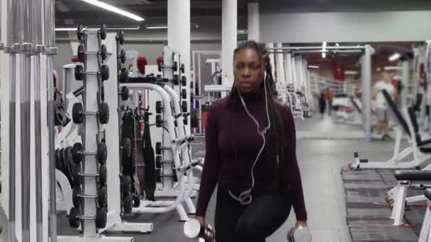 Sports training - black woman walks forwards and squats in the gym holding dumbbells — Stock Video