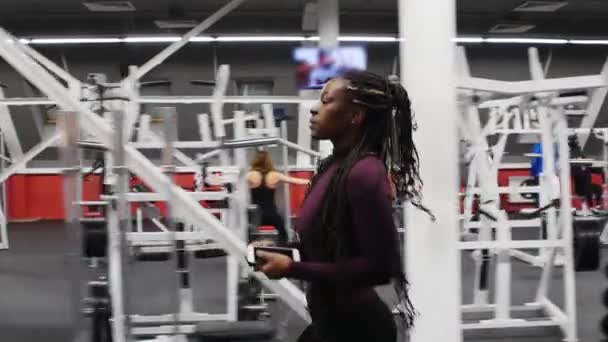 Sport training - zwarte vrouw loopt vooruit in de sportschool en zet haar hoofdtelefoon op — Stockvideo