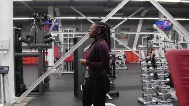 Спортивная тренировка в помещении - черная женщина идет вперед в спортзал и надевает наушники — стоковое видео