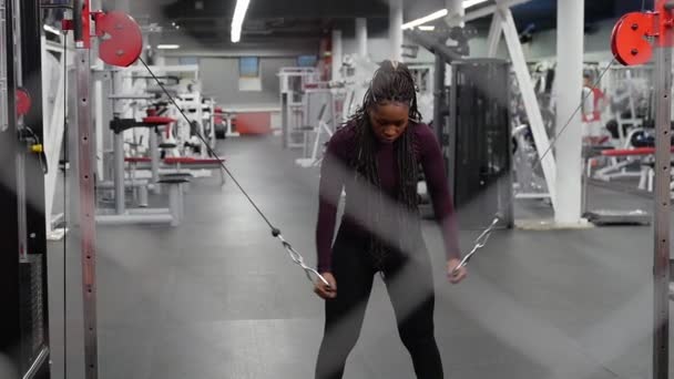 Спортивная тренировка - черная женщина тренирует руки с потянув держатели прикрепленные к весу и глядя вниз — стоковое видео