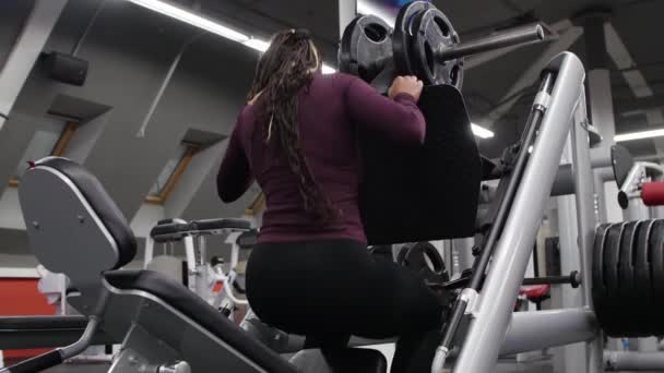 Sporttraining drinnen - schwarze Frau setzt sich auf ein Trainingsgerät und beginnt ihre Beine zu trainieren - Gewicht drücken — Stockvideo