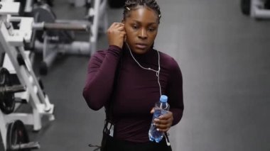 Spor eğitimi - siyah kadın boş salonda yürüyor ve şişeden su içiyor.