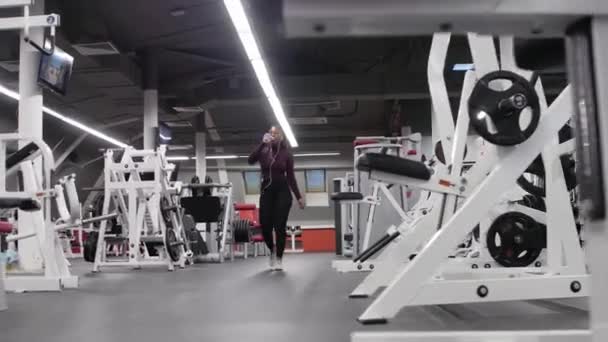 Sports training - african-american woman walks in the empty gym and drinking water — Stock Video