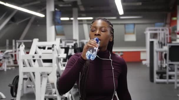 Sportovní trénink - černá atraktivní žena chodí do posilovny a pitnou vodu z láhve — Stock video