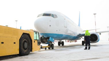 Kışın havaalanında duran büyük bir uçak. Uçağın yanında duran bir işçi.