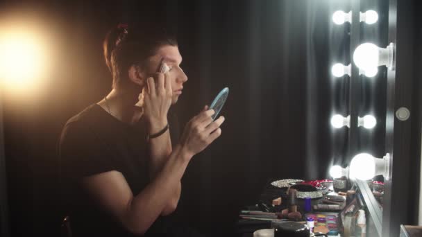 Drag καλλιτέχνης - νεαρός άνδρας βάζει μακιγιάζ πίσω από τις σκηνές μπροστά από έναν καθρέφτη — Αρχείο Βίντεο
