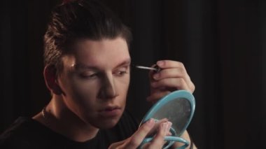 Sürükleme sanatçısı - genç adam kaşlarını yapıştırıyor ve yere seriyor.