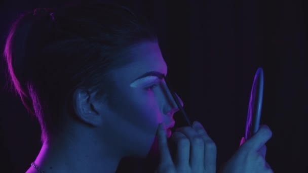 Drag artist - giovane uomo che disegna nuove sopracciglia e si guarda allo specchio - illuminazione al neon — Video Stock