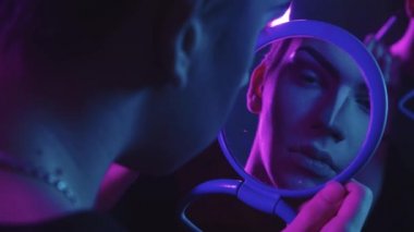 Sürükleme sanatçısı - gözlerine temel renk uygulayan genç adam - mavi ve mor neon ışıklı