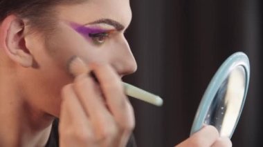 Sürükleme sanatçısı - genç adam fırça kullanarak gözlerinin altından kabartma tozu çıkarıyor.