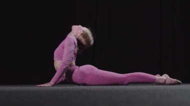 Genç bayan jimnastikçi antrenmandan önce ısınıyor. Sırtını dairesel hareketlerle ısıtıyor.