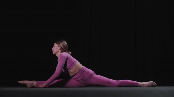 Young female gymnast sits on splits and leaning forwards for her toes — Stock Video