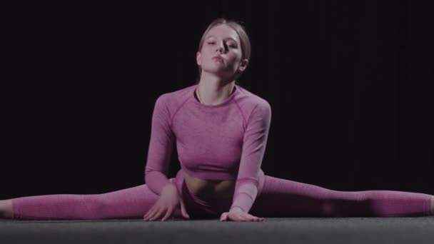 Joven gimnasta femenina se sienta en divisiones y se inclina hacia adelante — Vídeos de Stock