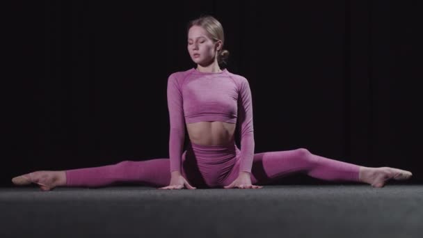 Young female gymnast in pink clothes sits on splits and leaning forwards for her toes — ストック動画