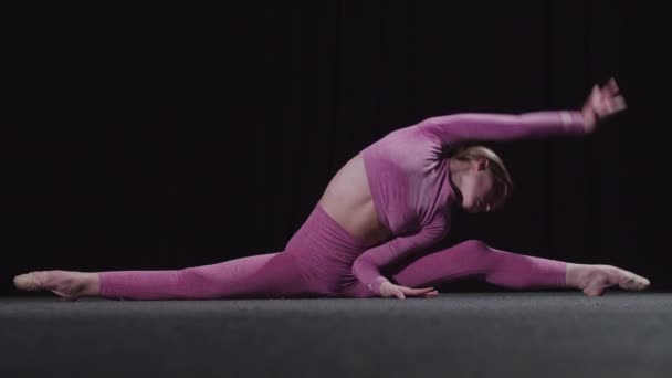 Young female gymnast sits on splits - bending her knees a little and leaning forwards for her toes — Stock Video