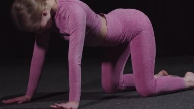 Genç bayan jimnastikçi antrenman için ısınıyor. Sırtını ve belini eğiyor.