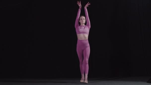 Ung vacker blond kvinnlig gymnast utför en gymnastisk övning i svart studio — Stockvideo